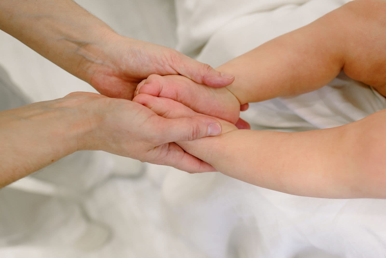Les mains d'une praticienne accompagnent la main d'un nourrisson lors d'une séance sensori-motrice.