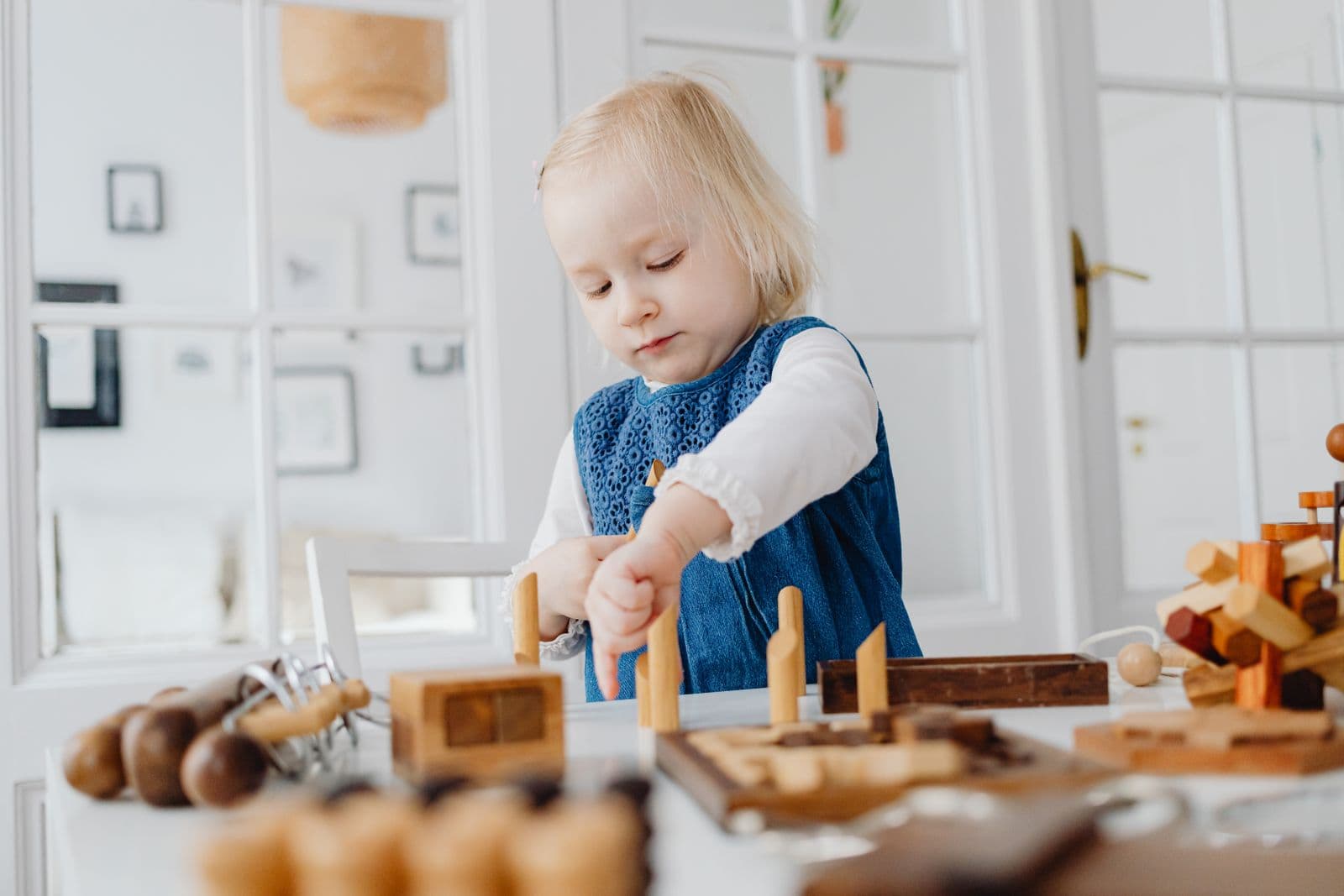 Une jeune enfant concentrée manipule des jouets en bois sur une table.