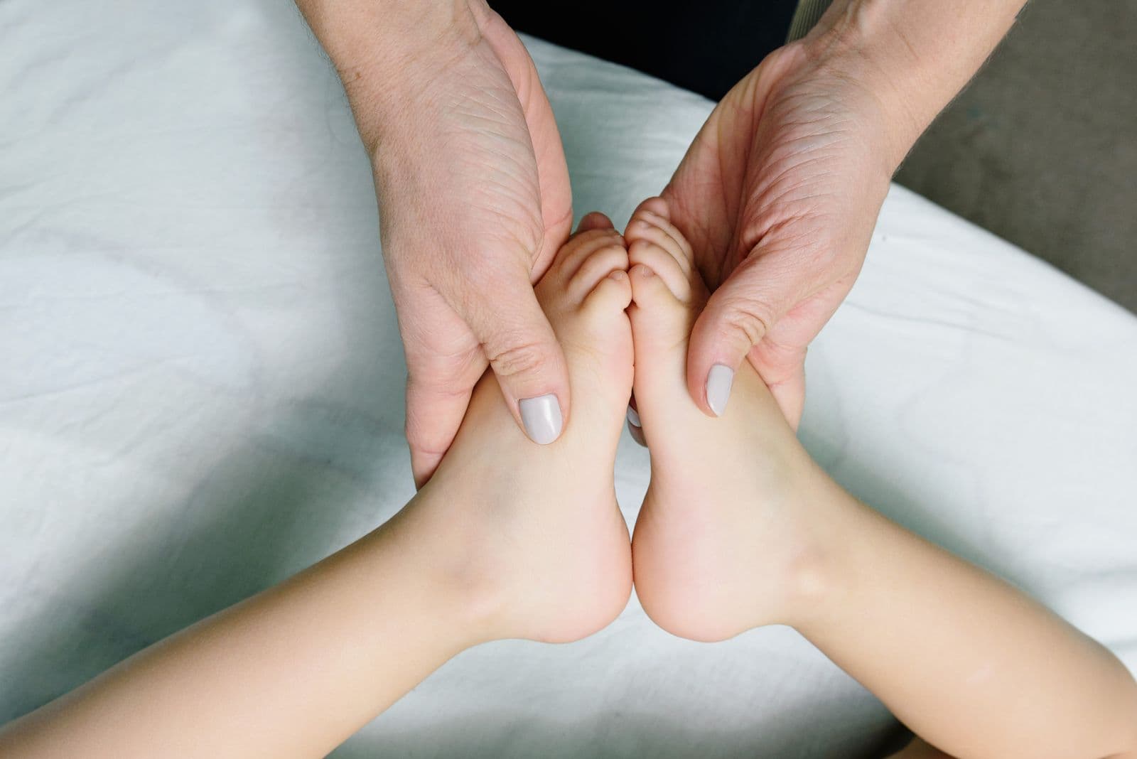 Les mains d'une praticienne mobilisent doucement les pieds d'un jeune enfant.